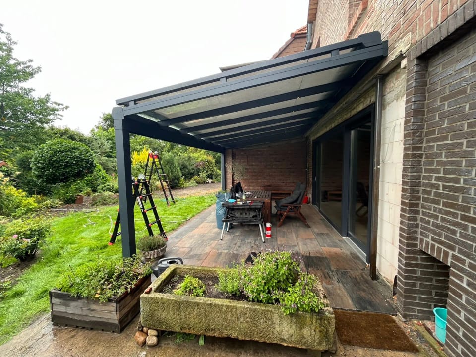 Von unserem Team montiertes Terrassendach in Anthrazit mit Glasdach über einer Holzterrasse am Klinkerhaus