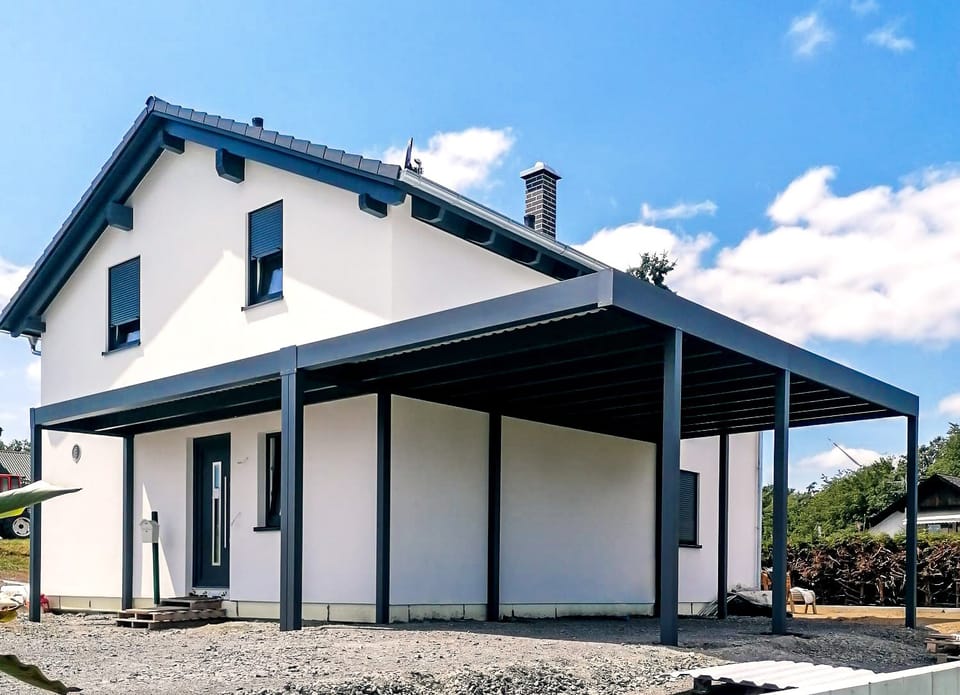 Anthrazitfarbener Aluminium-Carport an einem weißen Einfamilienhaus